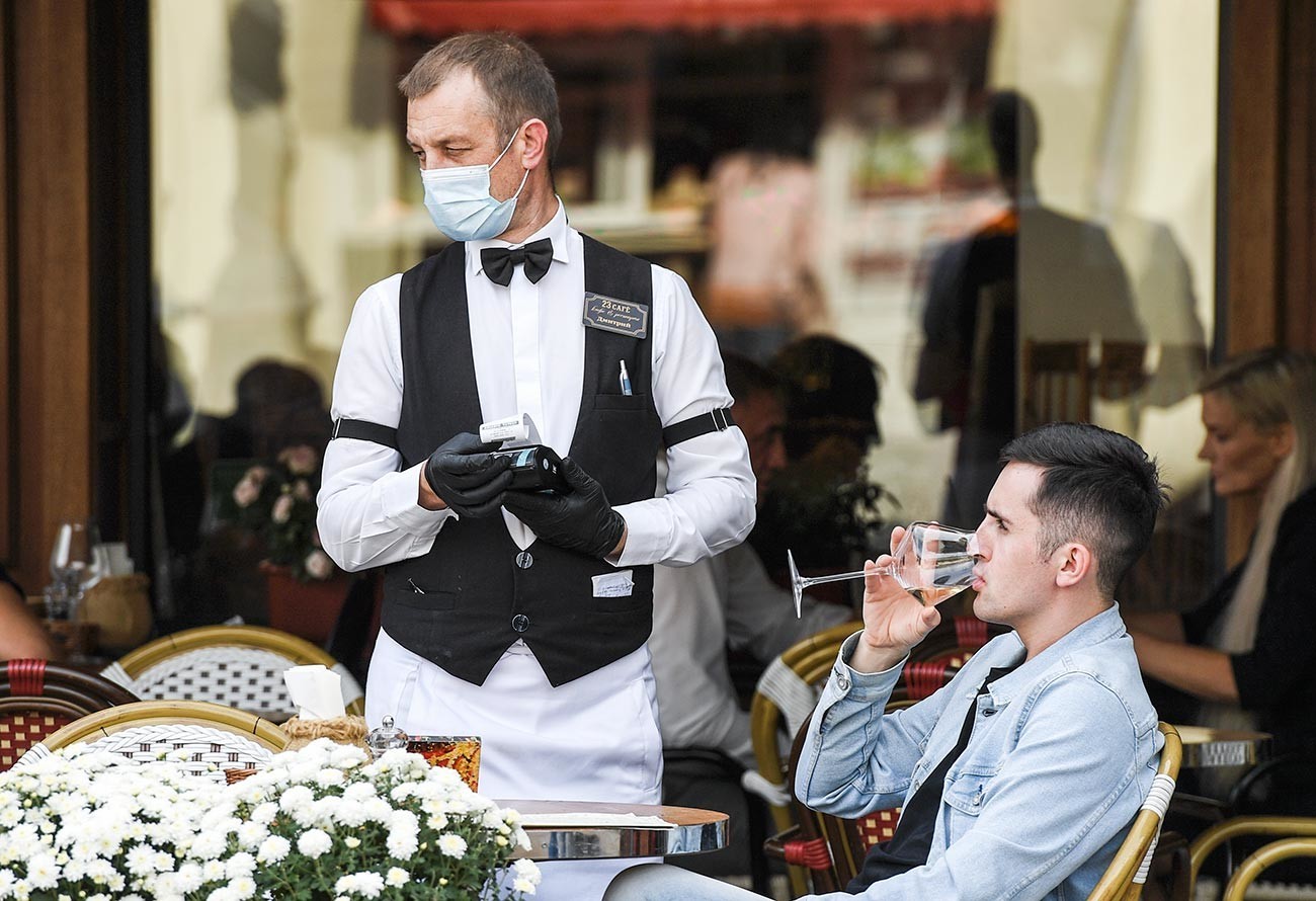 Natakar v zaščitni maski sprejema naročilo mladeniča v kavarni v Simferopolu.
