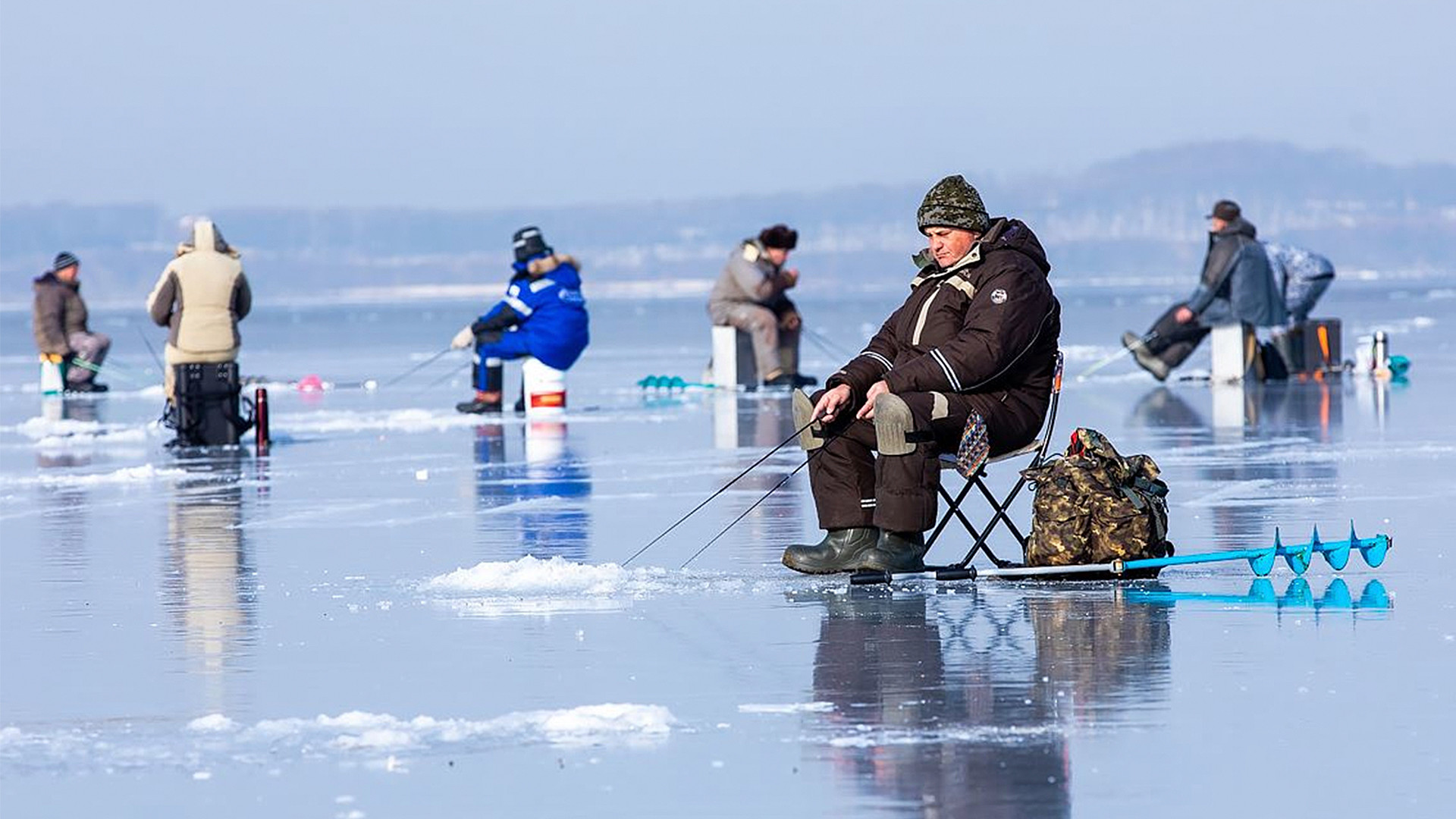 Cientos de agujeros en el hielo con pescadores sentados.