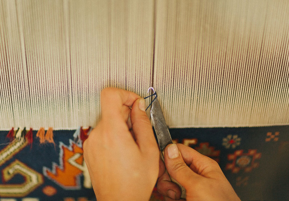 特別なフックを使用して、彼女たちはそれぞれの糸の周りに色付きの糸で作られた結び目を作る。これらの熟練職人の作業は驚くほど手際よい。