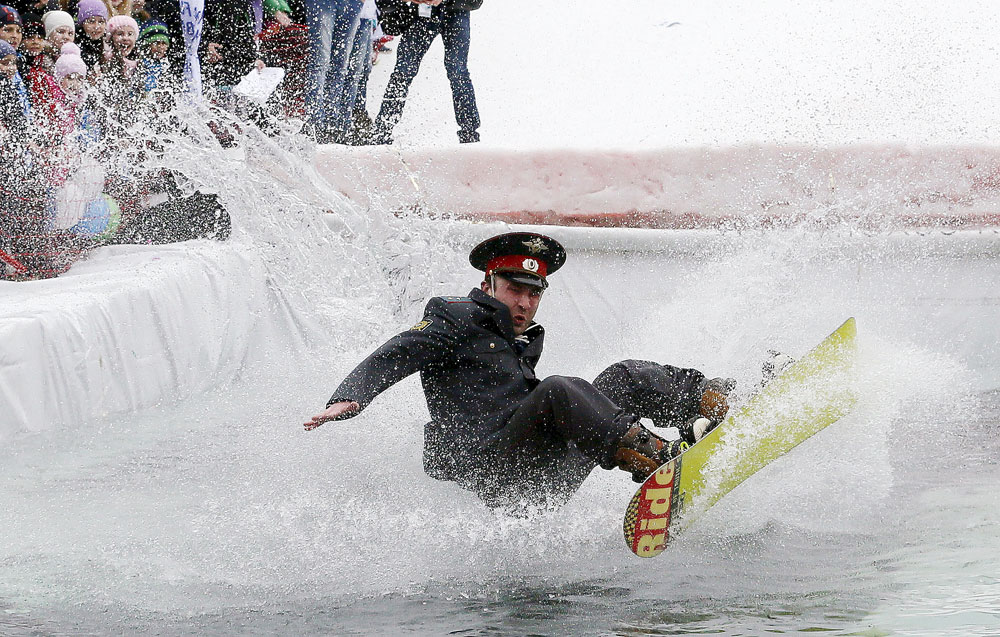 A snowboarder, wearing a costume of a Russian Interior Ministry officer, falls down in an attempt to cross a pool of water at the foot of a ski slope at the Bobrovy Log ski resort on the suburbs of the Siberian city of Krasnoyarsk, Russia